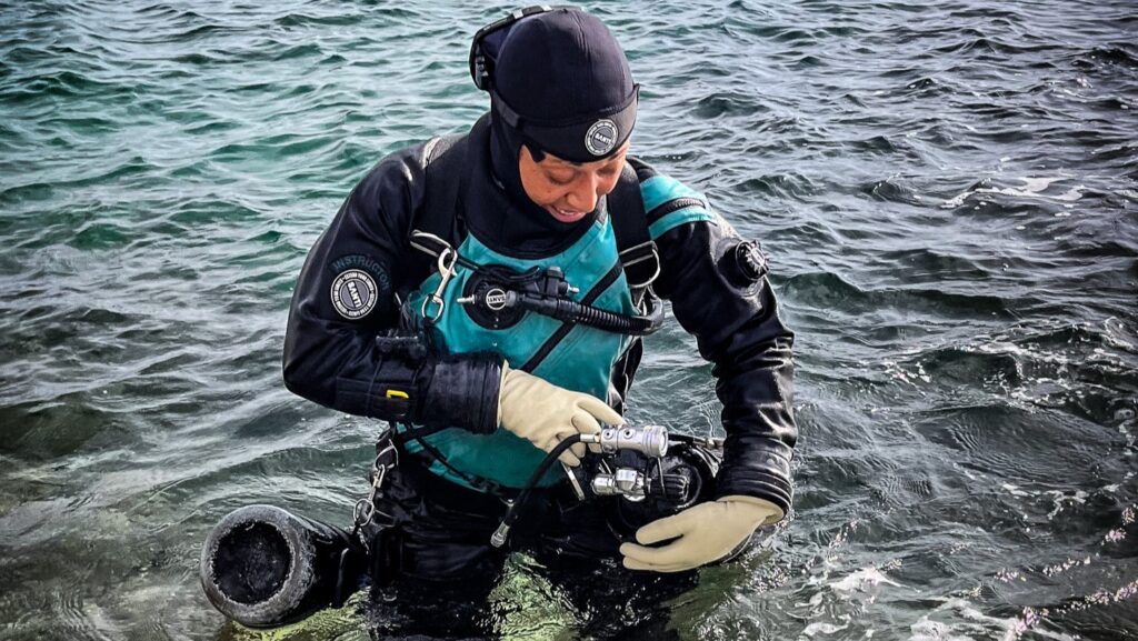 A scuba diver standing in shallow water and setting up sidemount configuration. Sidemount diving with Sidemount Society in Gozo (Malta)